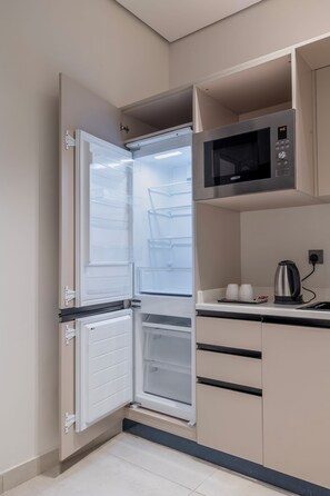 A compact kitchen with a built-in microwave, a kettle, and a refrigerator with multiple shelves. - Luxury Residential Serviced Apartments (Riyadh)