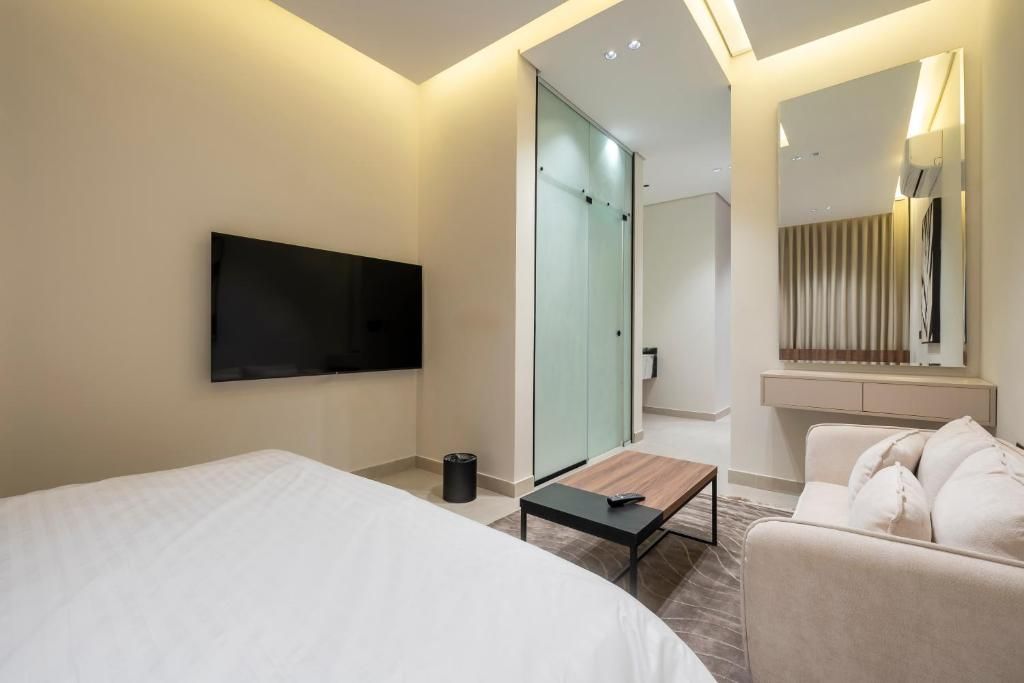 A modern hotel room with a bed, a flat-screen TV, a small table, a sofa, and a mirror.