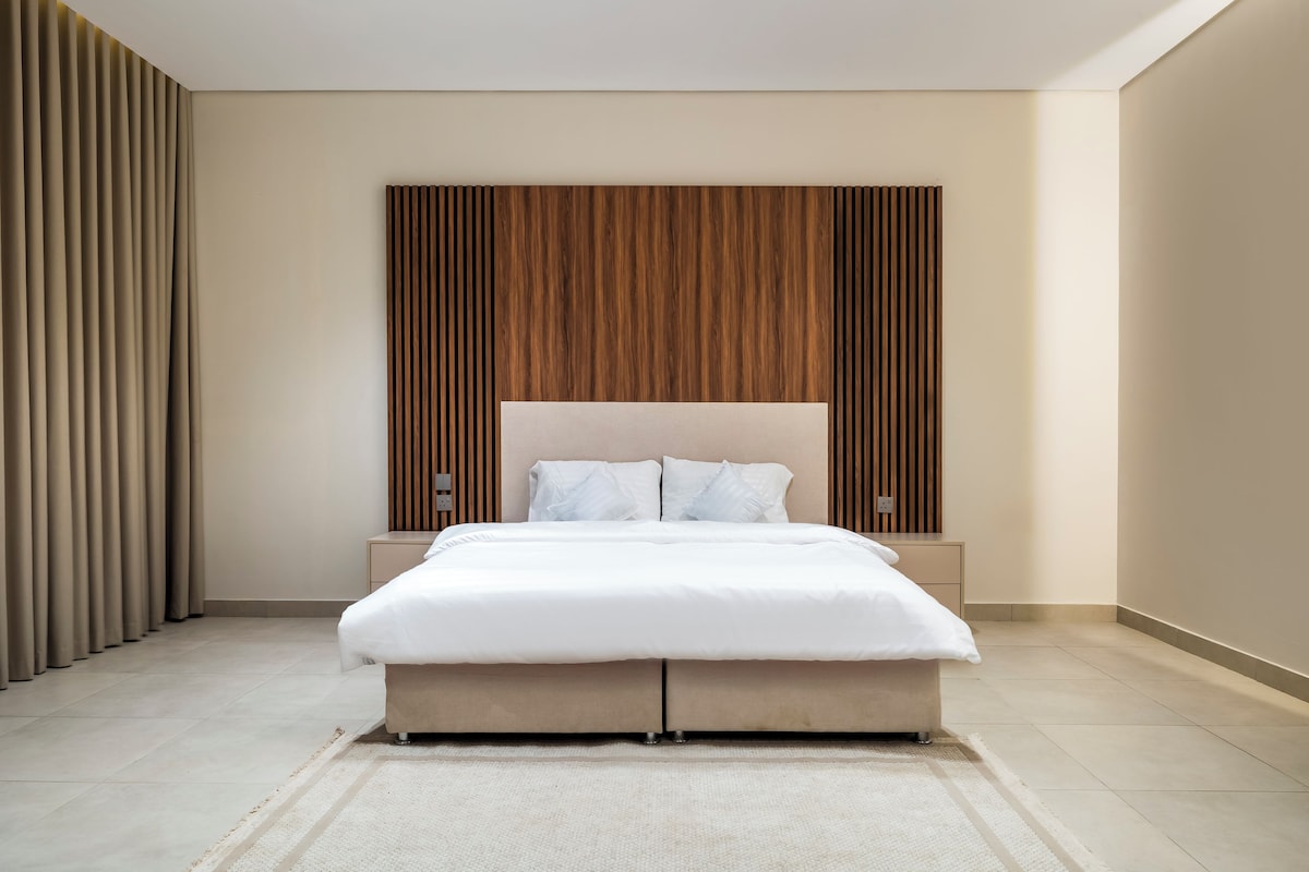 Un dormitorio moderno con una cama grande, un panel de pared de madera y un suelo de color claro.