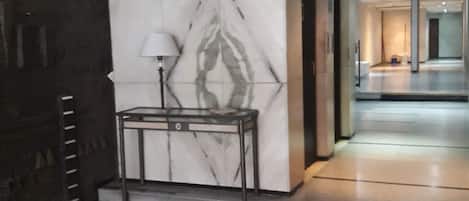 Un hall d’entrée avec un mur de marbre, une table avec une lampe et un couloir menant à une autre pièce.