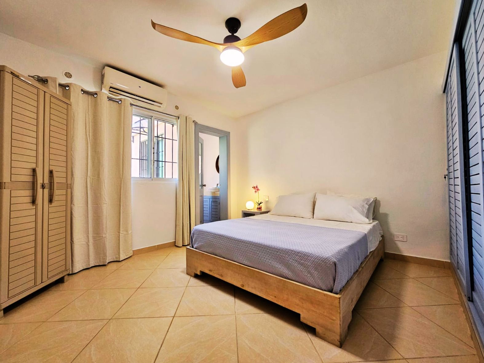 Un dormitorio con cama, ventilador de techo, ventana y armario.