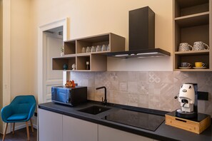Een moderne keuken met een zwart aanrecht, een inbouwoven, een koffieapparaat en een blauwe stoel.