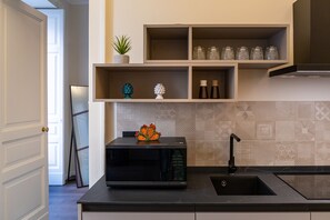 Een moderne keuken met een inbouwmagnetron, een spoelbak en decoratieve objecten op planken.