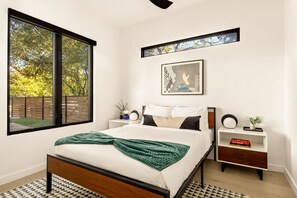 A bedroom with a large window, a bed with a green throw, a bedside table with a book, and a framed picture on the wall. - Eastside Swim - Pool, Spa, Movie Room - Sleeps 13 (Austin)