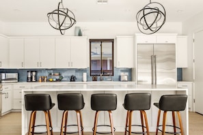 A modern kitchen with white cabinets, a large island with bar stools, and a stainless steel refrigerator. - Eastside Swim - Pool, Spa, Movie Room - Sleeps 13 (Austin)