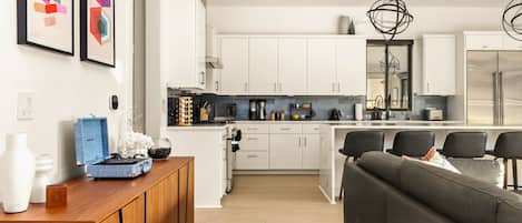 A modern kitchen with white cabinets, a central island, and a dining area with a dark sofa.
