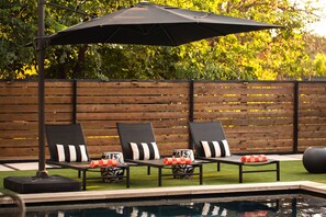 A poolside area with three lounge chairs, a table, and an umbrella. - Eastside Swim - Pool, Spa, Movie Room - Sleeps 13 (Austin)