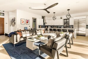 A modern living room with a sofa, coffee table, and chairs, a kitchen with white cabinets, and a ceiling fan. - Eastside Swim - Pool, Spa, Movie Room - Sleeps 13 (Austin)