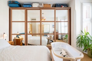 Ein Hotelzimmer mit großem Kleiderschrank, einem Babybett, einem Schreibtisch und einem Fenster mit Jalousien.