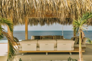 A beachside lounge with a sofa, palm trees, and a view of the sea. - Kas Secreto – An Exclusive Oceanfront Escape Villa in Bonaire (Kralendijk)