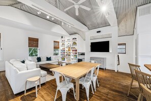 Een moderne woonkamer met een witte bank, een houten salontafel en een eethoek met een houten tafel en stoelen.