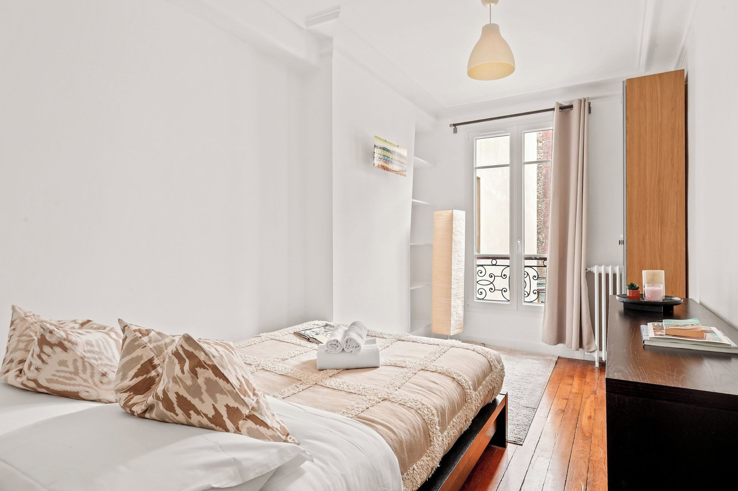 Een slaapkamer met een bed, nachtkastje, raam met gordijnen, radiator en hanglamp.