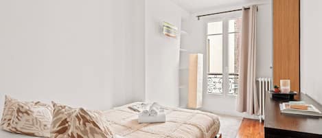 A bedroom with a bed, a bedside table, a window with curtains, a radiator, and a hanging light fixture.