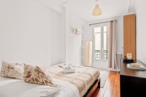 A bedroom with a bed, a bedside table, a window with curtains, a radiator, and a hanging light fixture. - Spacious 2BR - Eiffel Tower & Champ de Mars (Paris)