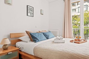 A hotel room with a bed, bedside table, lamp, and a view of the outside. - Spacious 2BR - Eiffel Tower & Champ de Mars (Paris)