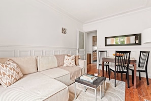 A living room with a sofa, a coffee table, and a dining area with chairs and a table. - Spacious 2BR - Eiffel Tower & Champ de Mars (Paris)