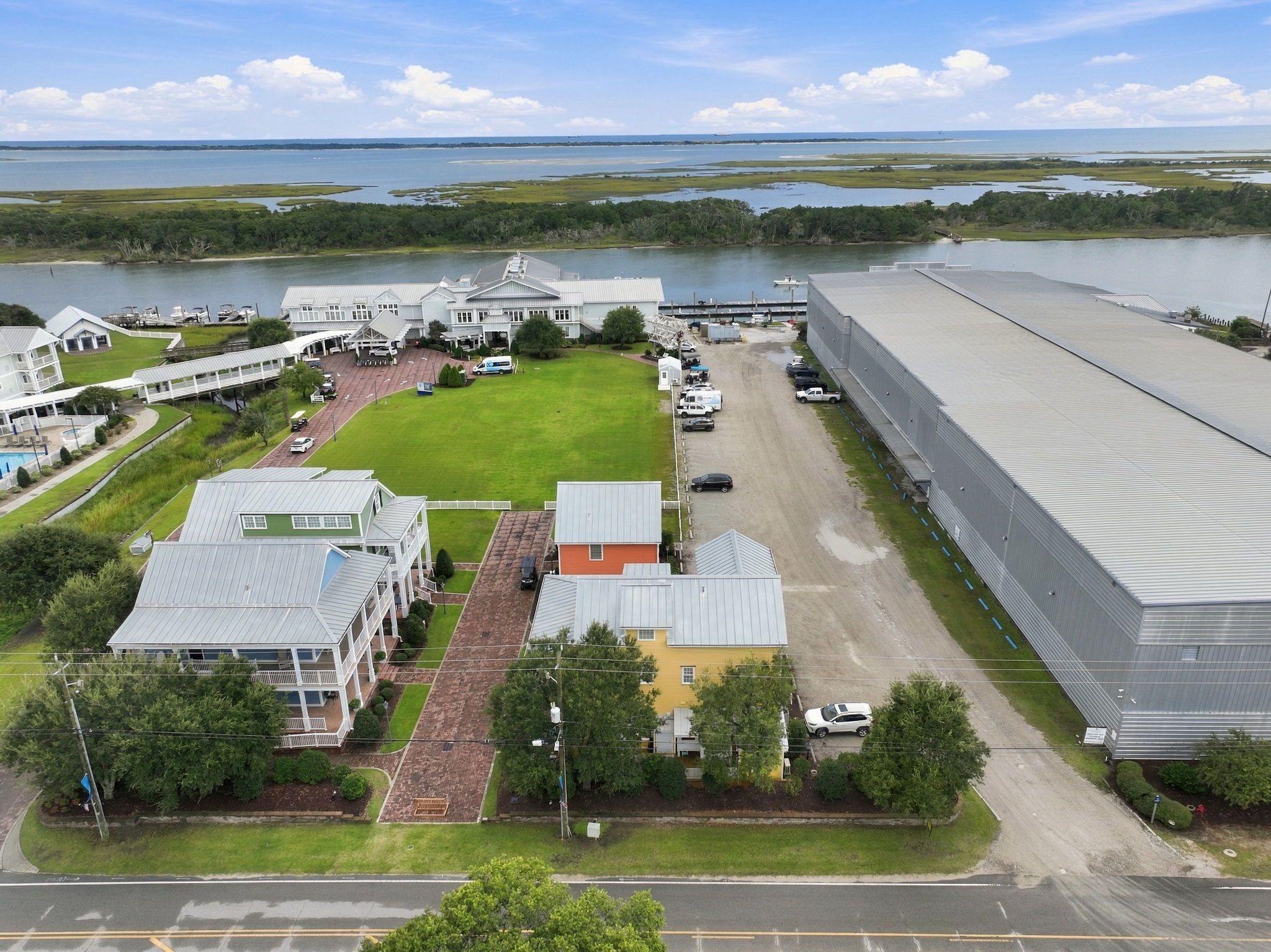 A large industrial facility with a parking area, a grassy field, and a body of water in the background.