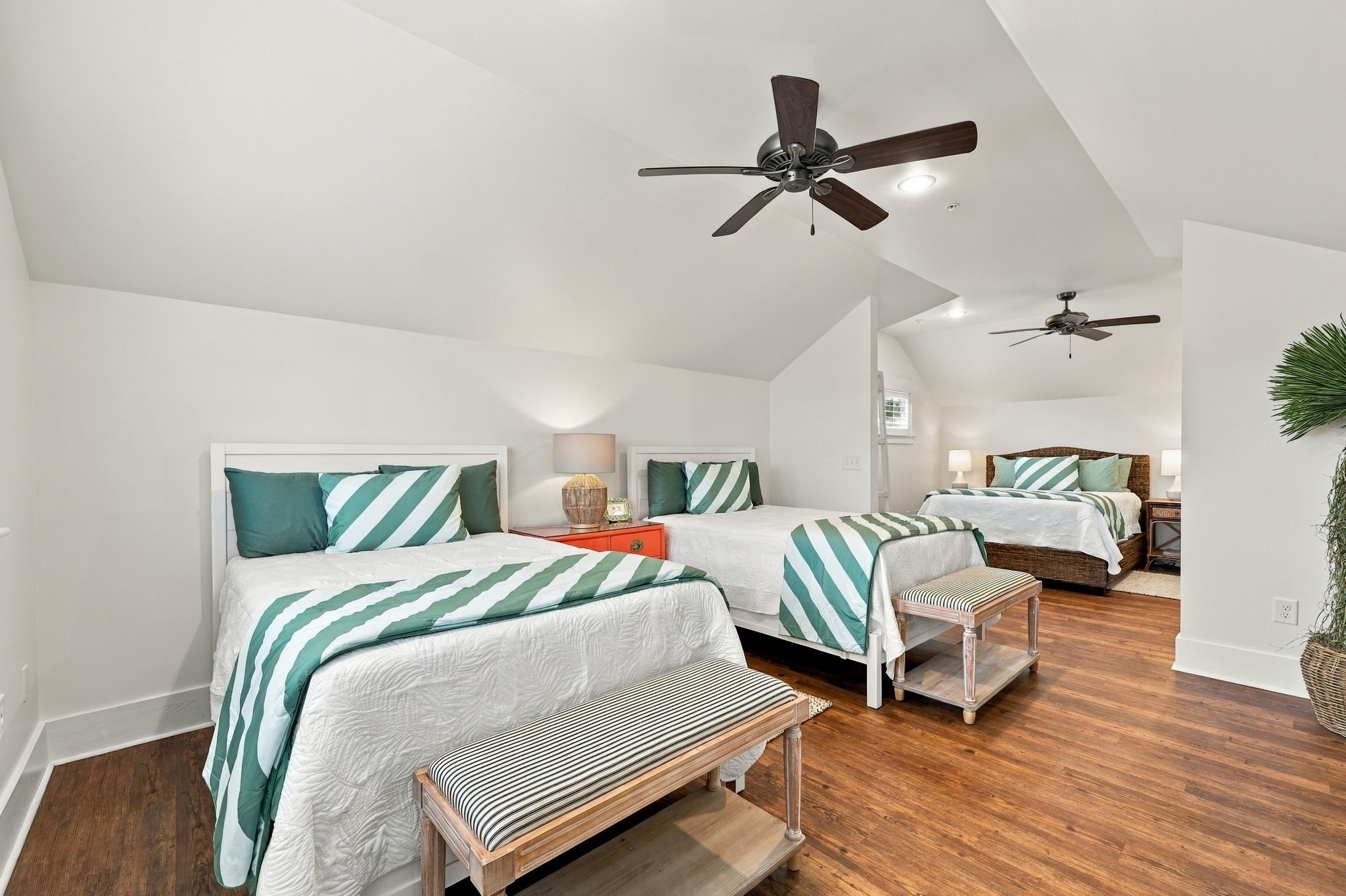 A bedroom with two beds, a ceiling fan, and a wooden bench.