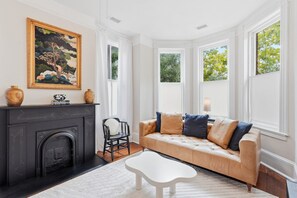 A living room with a fireplace, a sofa, a coffee table, and a painting on the wall. - Charming Victorian 2BR Near Forsyth (Savannah)