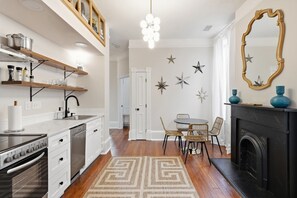 A modern kitchen with white cabinetry, a black stove, and a dining area with a round table and wicker chairs. - Charming Victorian 2BR Near Forsyth (Savannah)
