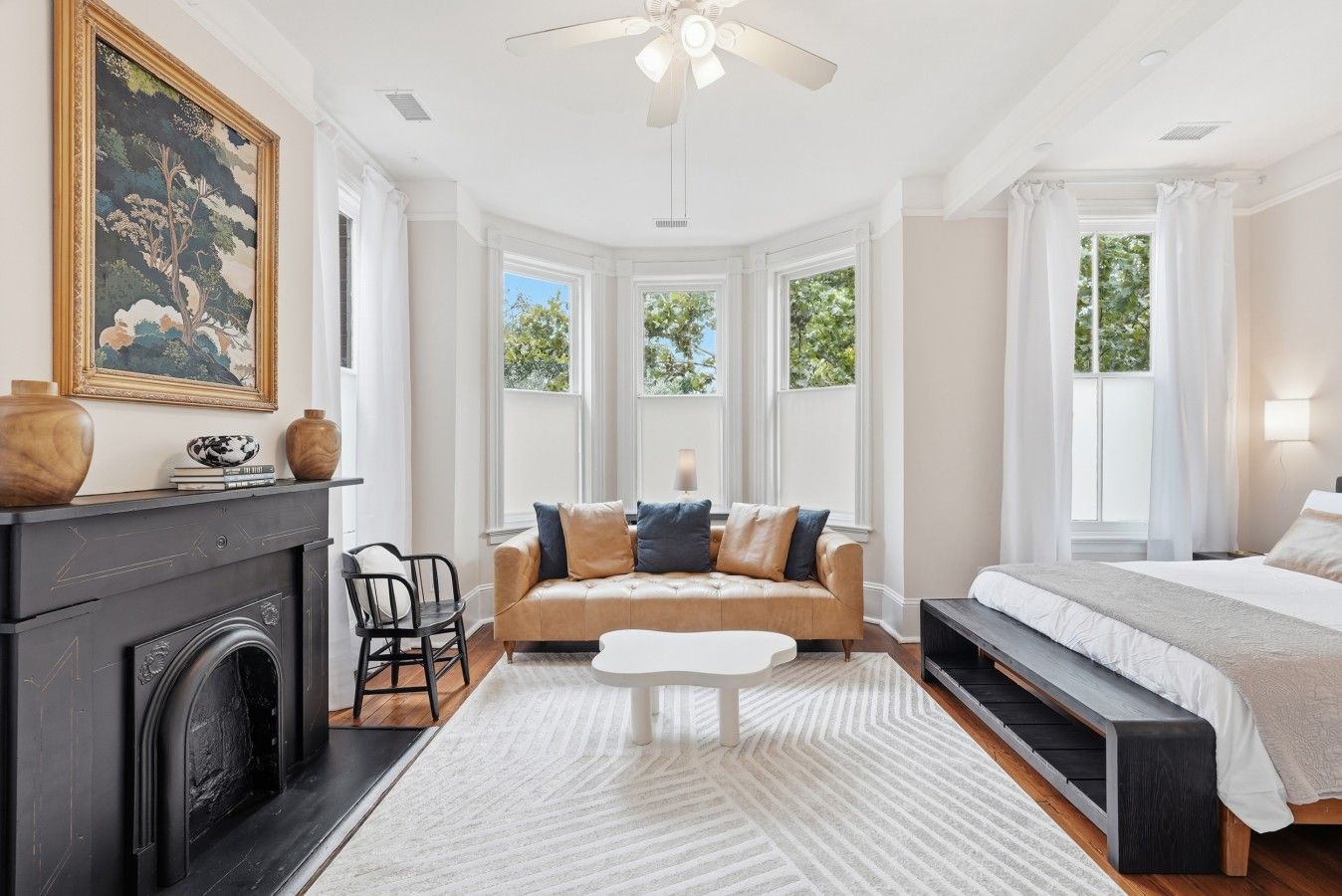 A bedroom with a bed, a sofa, a fireplace, and a large window.