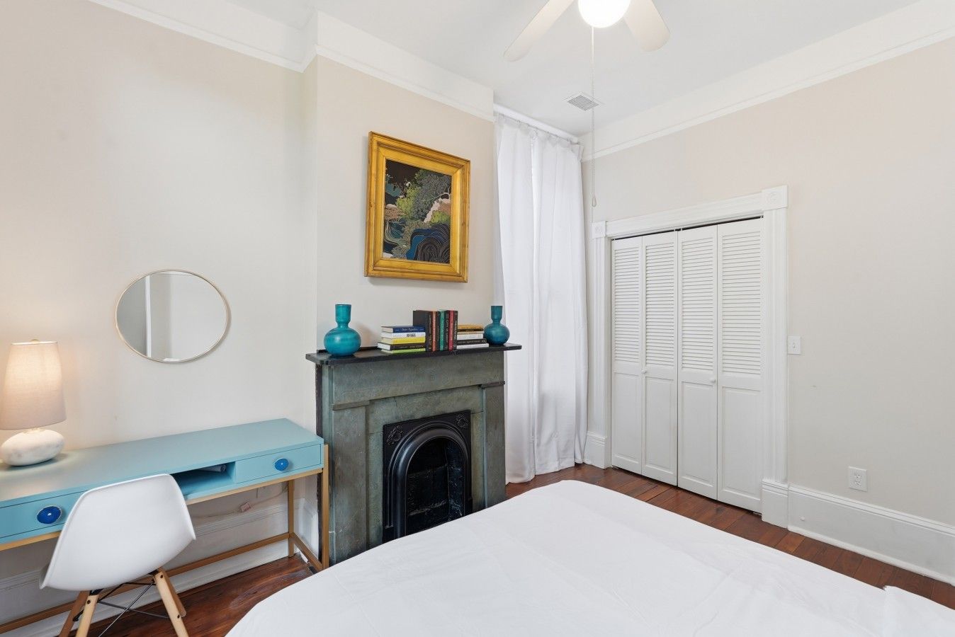 Een slaapkamer met een bed, een bureau met stoel, een open haard, een kledingkast en een plafondventilator.