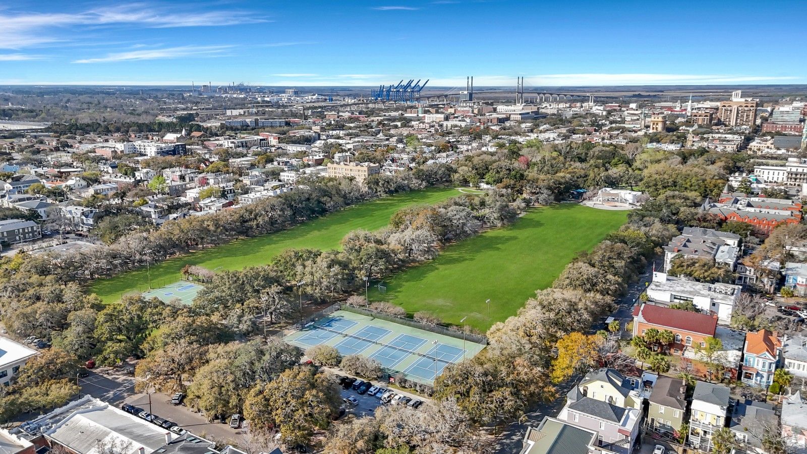 An aerial view of a residential area with multiple tennis courts, houses, and a distant industrial area.