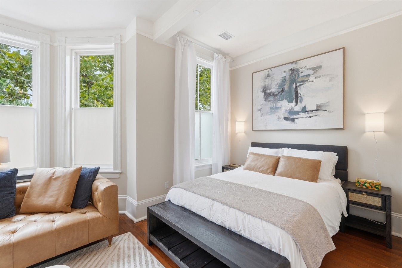 A bedroom with a bed, bedside tables, a bench, and a large abstract painting.