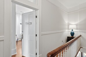 A hallway with a white door, a wooden staircase, and a blue vase on a small table. - Charming Victorian 2BR Near Forsyth (Savannah)
