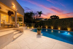 A modern outdoor pool area with a clear view of the sky, a well-lit patio with seating, and a neatly trimmed hedge. - Hillside City-View Retreat with Pool & Alfresco, Near City (Dianella)