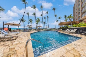A swimming pool with lounge chairs and umbrellas, surrounded by palm trees and a hotel building. - Mana Kai 310: 2  BR, 2  BA Condominium in Kihei, Sleeps 4 (Kihei)