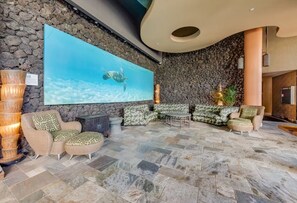 A lobby with a stone wall, a large blue mural of a turtle, and a seating area with patterned sofas and chairs. - Mana Kai 310: 2  BR, 2  BA Condominium in Kihei, Sleeps 4 (Kihei)