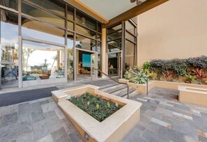 A modern building entrance with glass doors, a staircase, and a landscaped area with plants. - Mana Kai 310: 2  BR, 2  BA Condominium in Kihei, Sleeps 4 (Kihei)