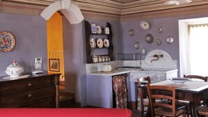 A room with a dining table, chairs, a kitchen area with a marble countertop, and decorative plates on the wall. - Ca' San Sebastiano Wine Resort & Spa 2 (Castel San Pietro)