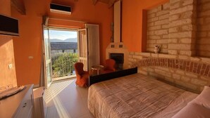 A bedroom with a bed, a fireplace, a balcony with a view, and a stone wall. - Ca' San Sebastiano Wine Resort & Spa 2 (Castel San Pietro)