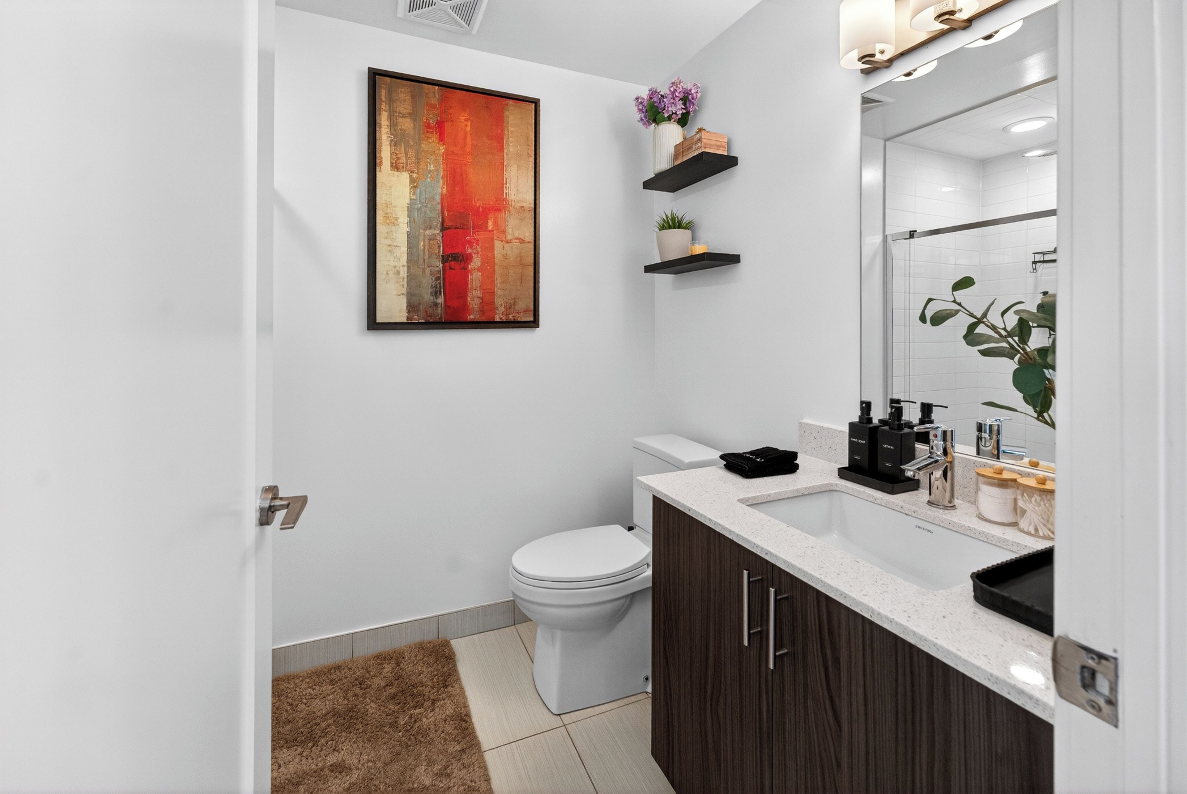 A modern bathroom with a white toilet, dark wooden cabinets, a white sink, and a large mirror.