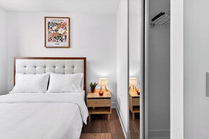 Ein Hotelzimmer mit einem Bett, einem Nachttisch mit Lampe, einem gerahmten Bild an der Wand und einem Holzboden.