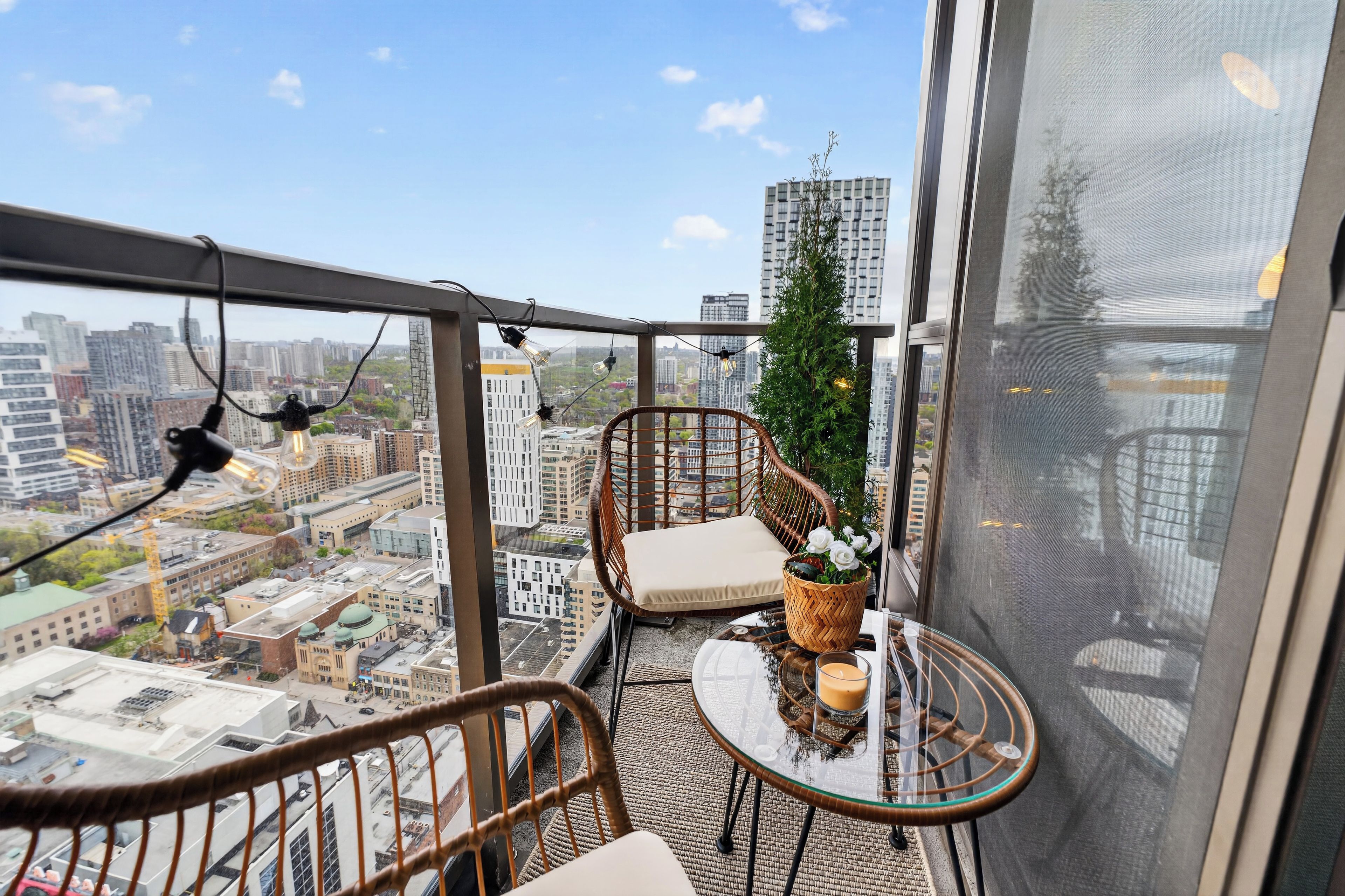 Een balkon met rieten meubels, een glazen tafel en uitzicht op de stad.