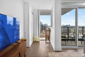 Ein modernes Wohnzimmer mit einem großen Flachbildfernseher, einer Holzkonsole und Blick auf die Stadtlandschaft durch eine große Schiebeglastür.