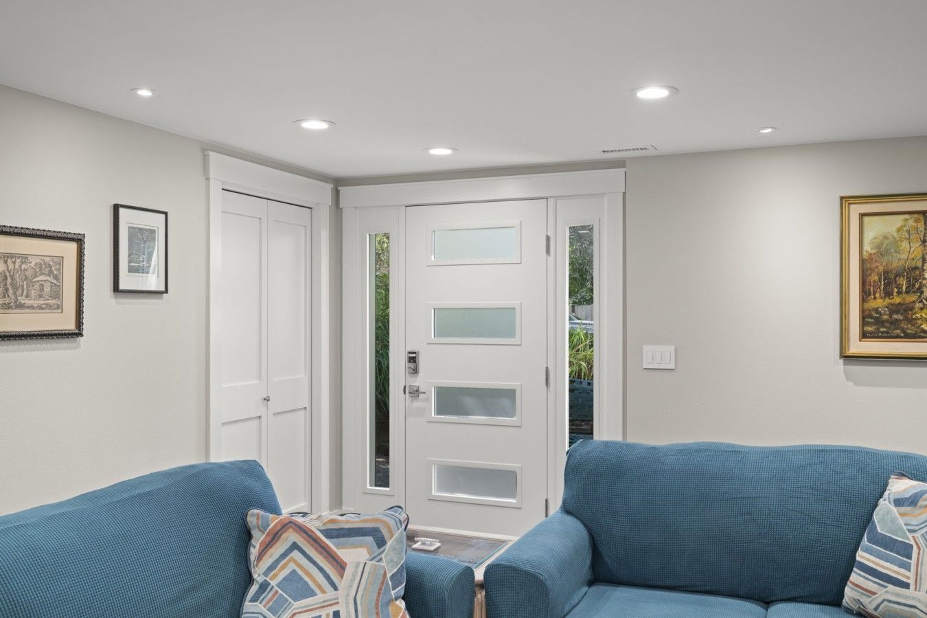 Una habitación con una puerta blanca, dos sofás azules y un cuadro en la pared.