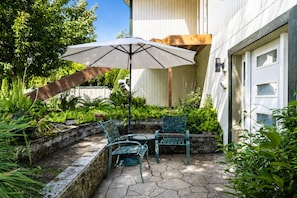 An outdoor patio with a table and chairs, a large umbrella, and a stone wall. - Serene Kenmore Stay - 2BR, Patio & Parking (Kenmore)