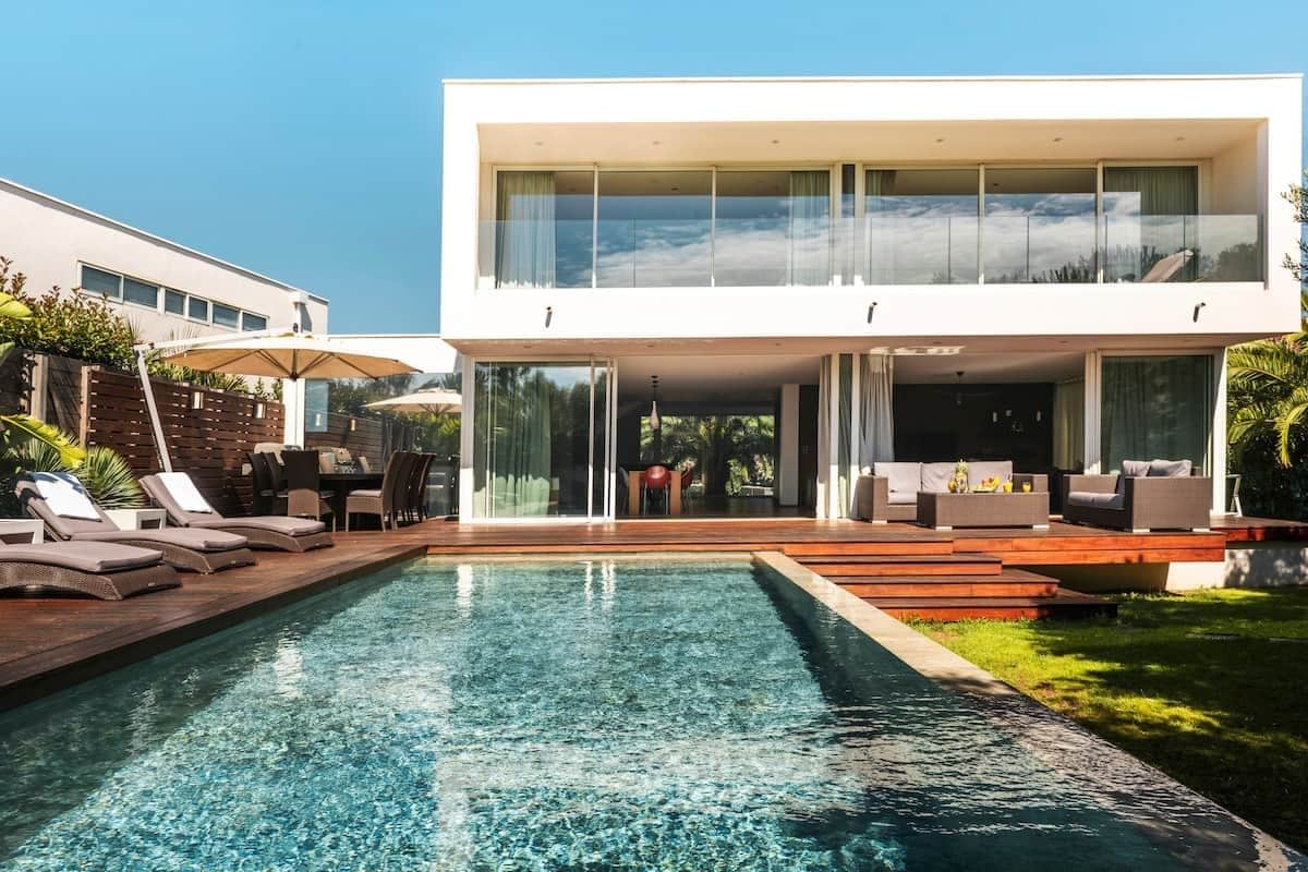 A modern two-story house with a swimming pool, outdoor seating, and a view of the sky.