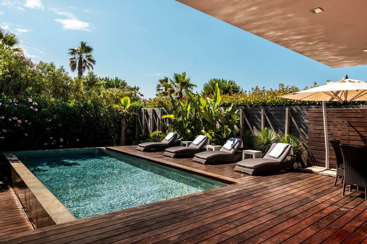 A wooden deck with a swimming pool, lounge chairs, and a table with an umbrella.