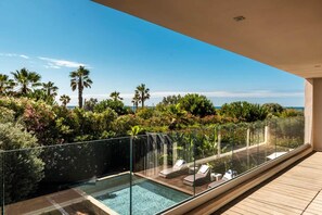 Ein Dachpool mit Infinity-Kante, ausgestattet mit Liegestühlen, umgeben von üppiger Vegetation und Palmen, mit Blick auf einen klaren, blauen Himmel.