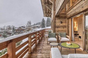 Eine Holzdar Terrasse mit Holzwand, eine Sitzgelegenheit mit Stühlen und Tisch, und ein Blick auf schneebedeckte Häuser im Hintergrund.