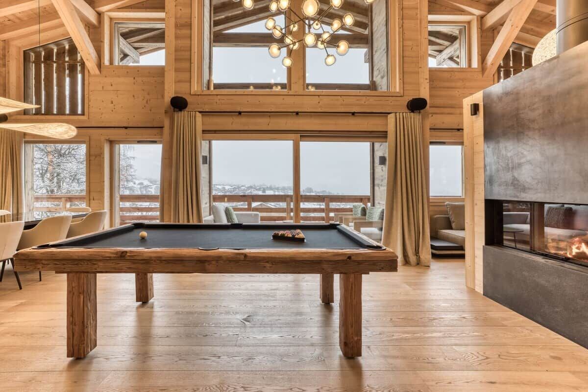 A spacious room with a pool table, large windows, and a fireplace.