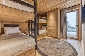 Ein Zimmer mit Etagenbetten, Holzboden, einem großen Fenster mit Vorh ängen und einem runden Teppich.