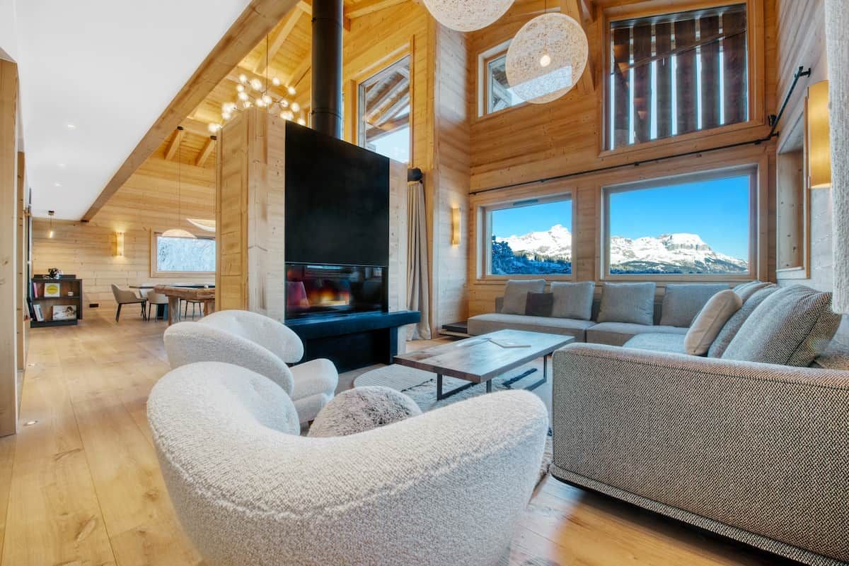 A spacious living area with a fireplace, large windows, and a high ceiling.