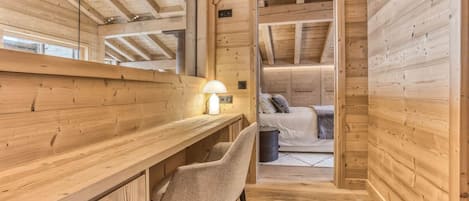 A wooden interior with a desk, chair, and a bed in the background.