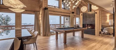 Une pièce spacieuse avec une table de billard, un plancher en bois, de grandes fenêtres et une cheminée.